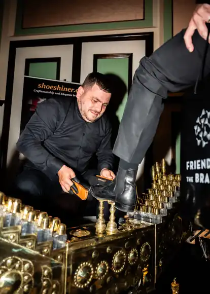 A black boot receiving care by hand at the brass shoeshine box.